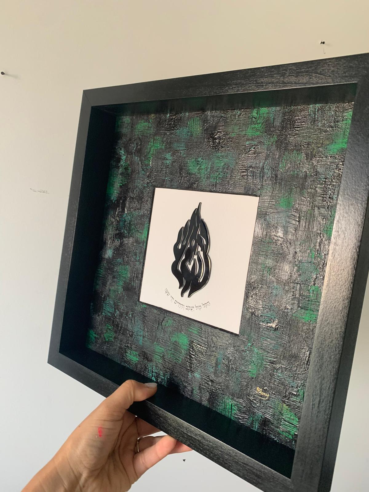 Breslev green and black framed artwork held in hand, Na Nach Nachma flame on dark painted background, modern Jewish wall decor